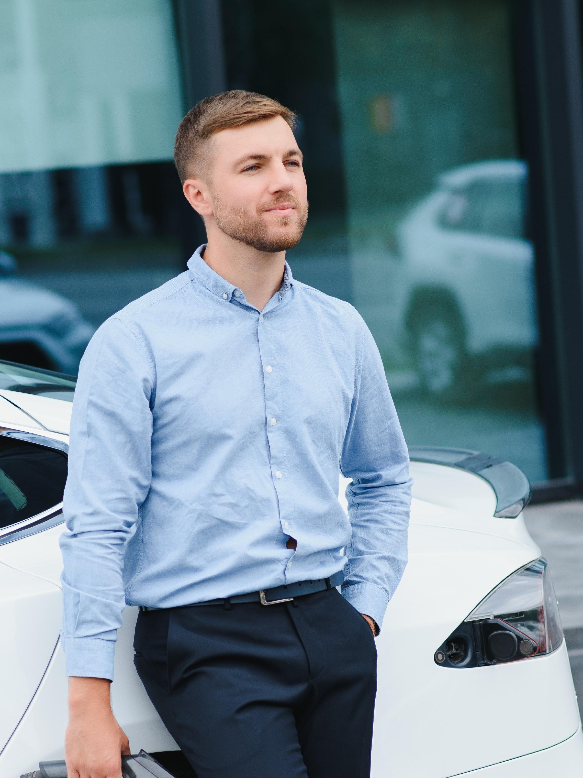 Mann lehnt sich an sein Elektro-Auto und hält Ladekabel in der Hand