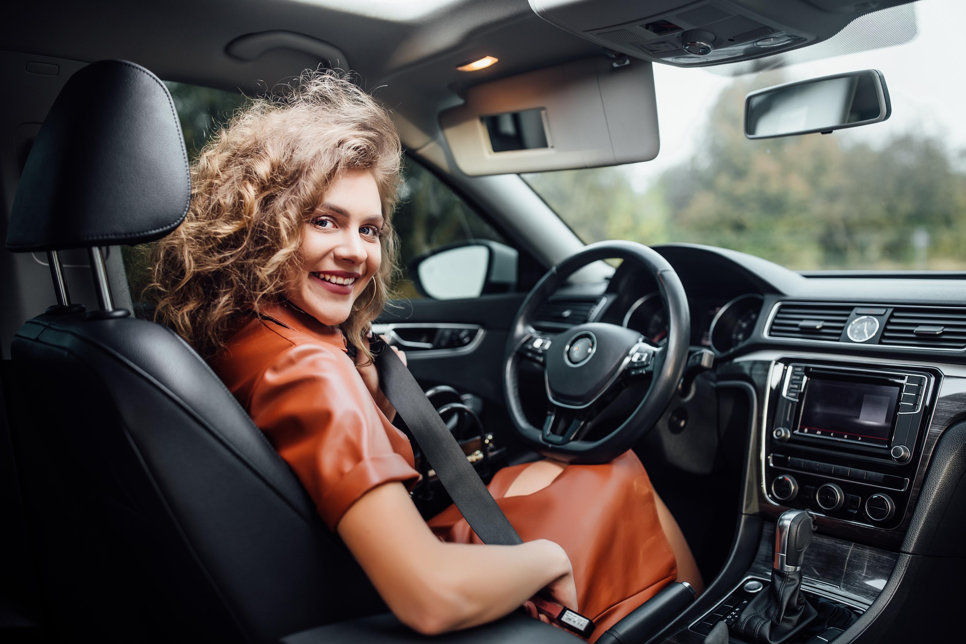 Eine Frau sitzt auf dem Fahrersitz in einem Auto und schnallt sich gerade an.