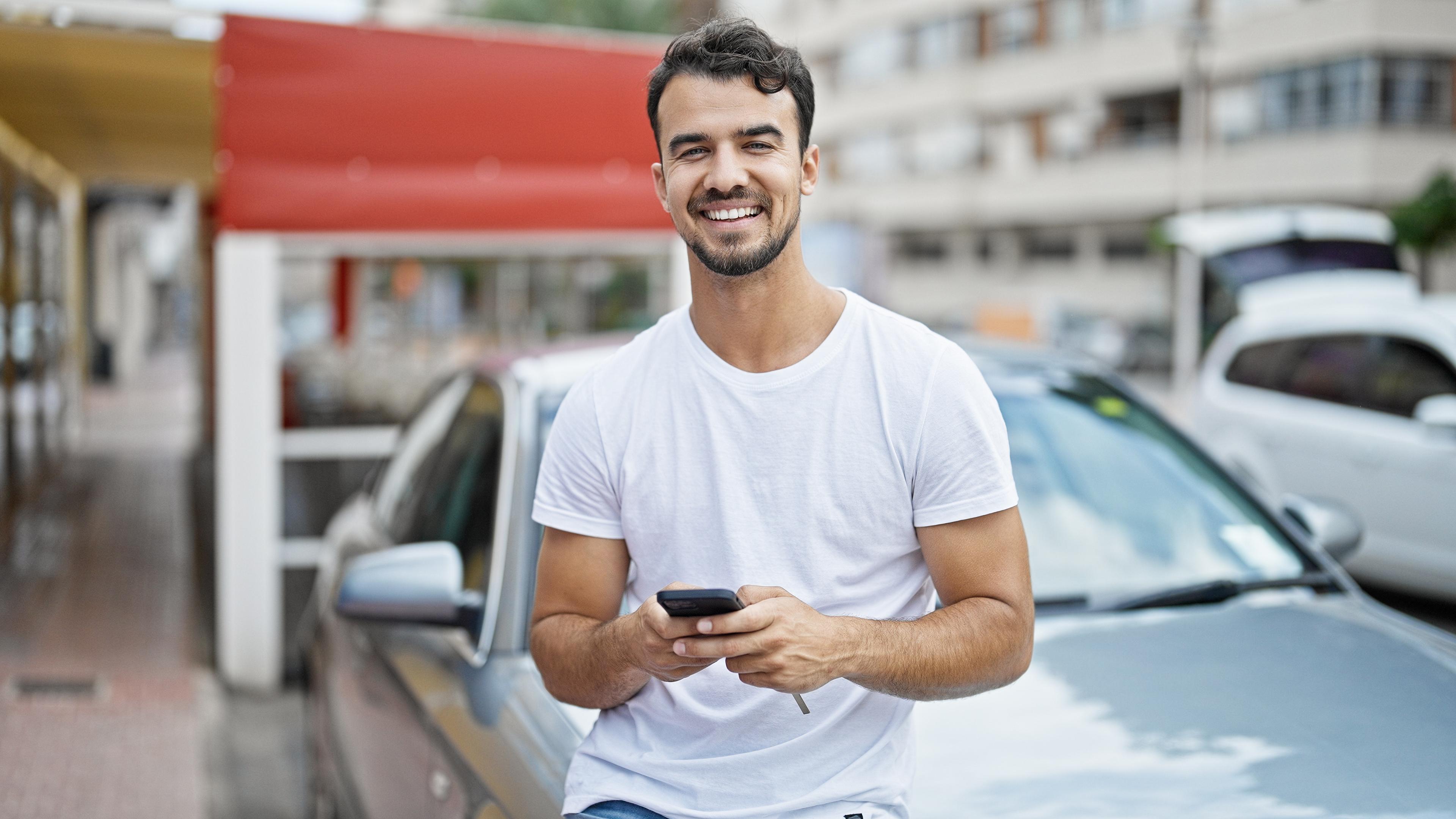 Mann sitzt mit Handy auf Motorhaube