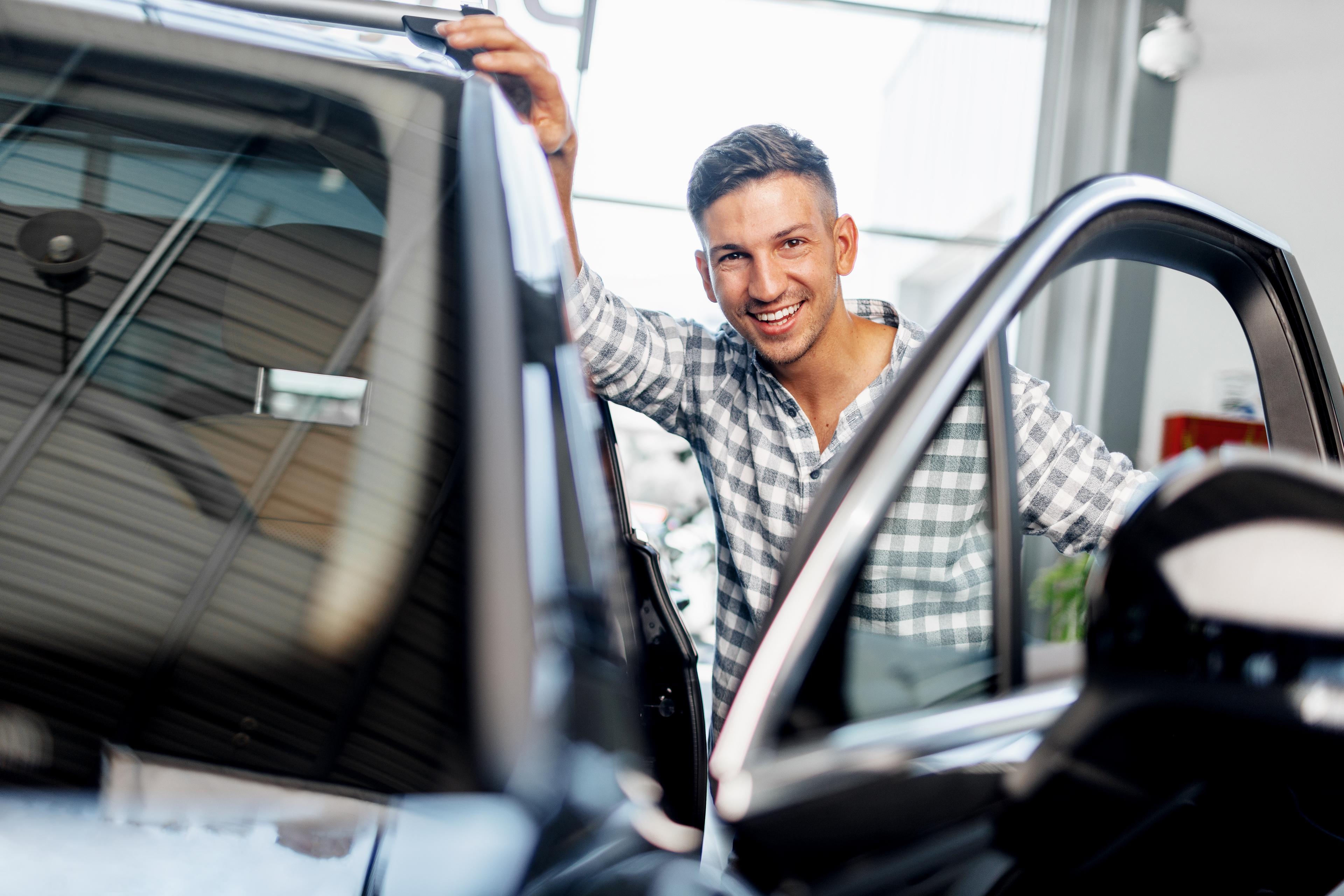 Mann öffnet eine Autotür und blickt in die Kamera