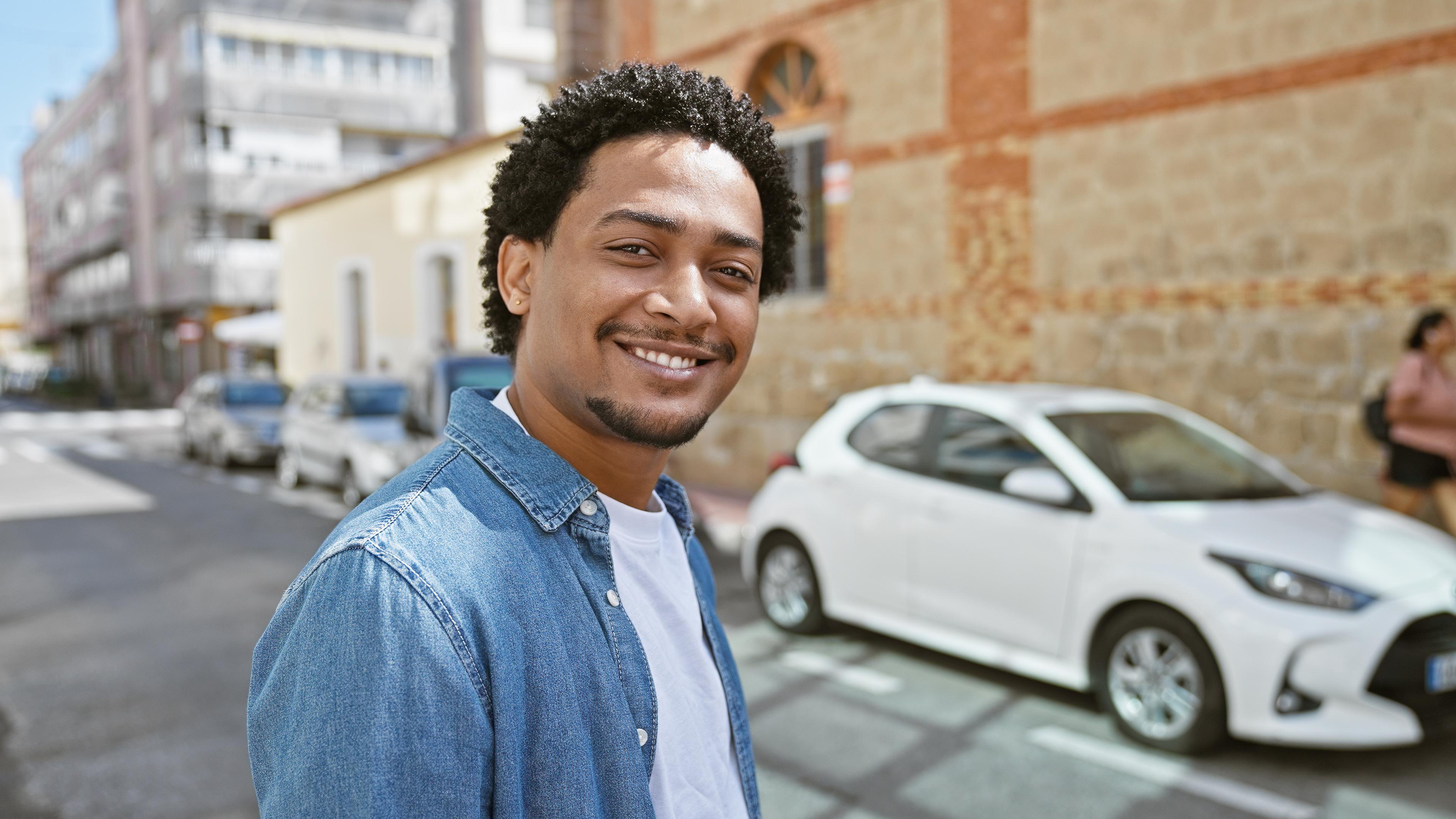 Ein junger Mann steht vor einem weißen Auto