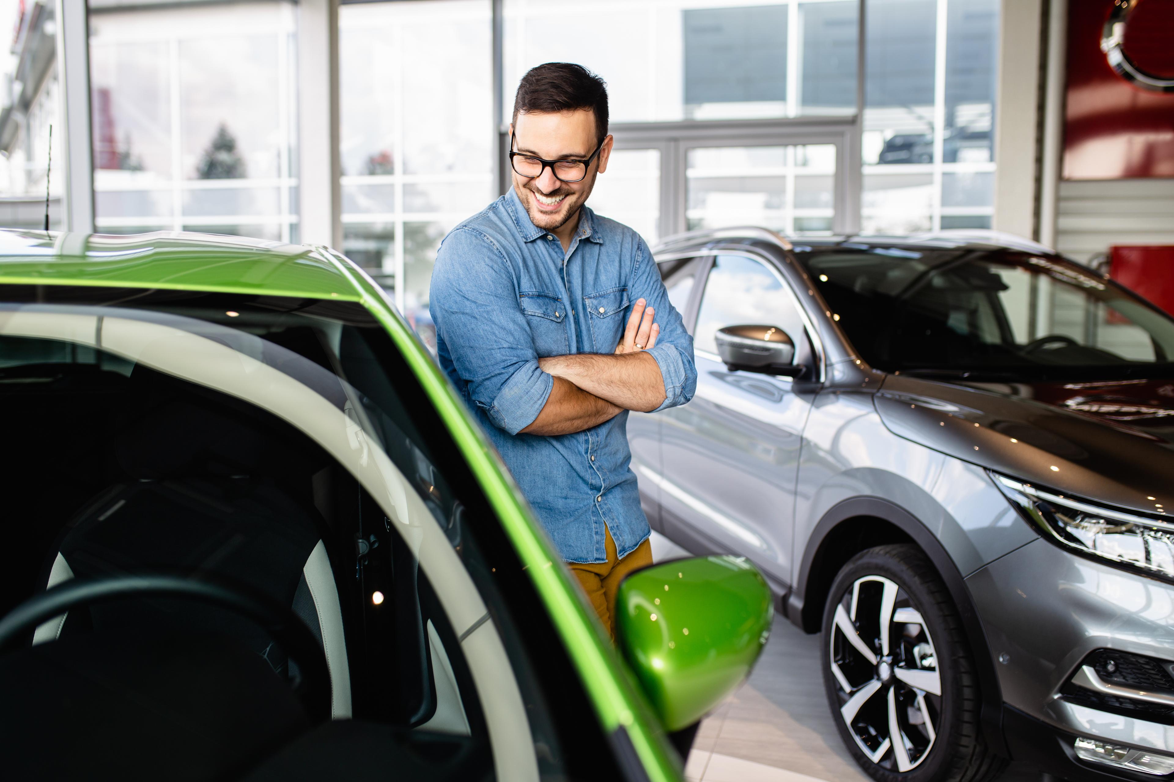 Mann blickt mit einem Lachen auf ein grünes Auto